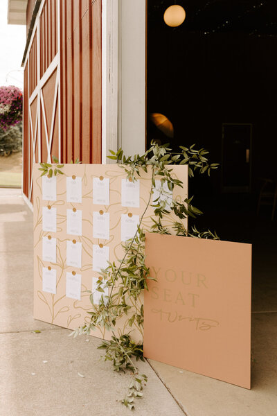 Pink wedding seating chart combo featuring florals and hand-drawn flowers sitting out front of a wedding barn in Oregon representing full service design and calligraphy by Life in Letters.