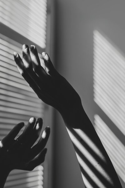Two hands reaching in front of window with sun light streaming in all in black and white
