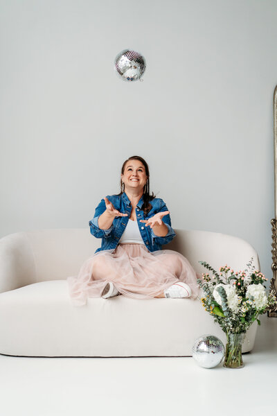 Female in jean jacket and light pink skirt kicking leg up on a couch.