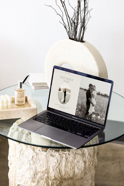 Computer sitting on glass table next to perfume and cream decor
