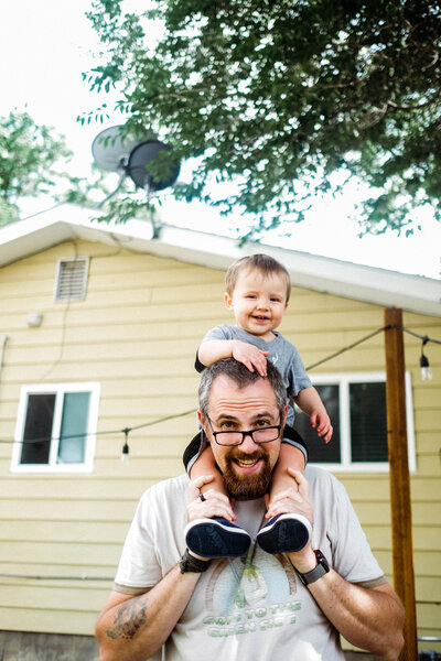 A toddler, Howie, riding on his  dad's shoulders smiling