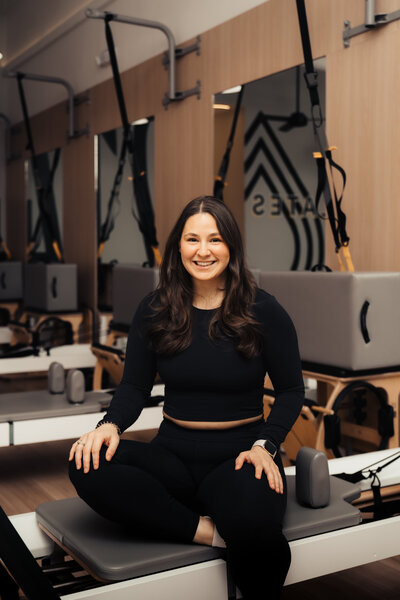 Headshot of Pilates instructor  standing in front of Pilates214 neon logo sign.