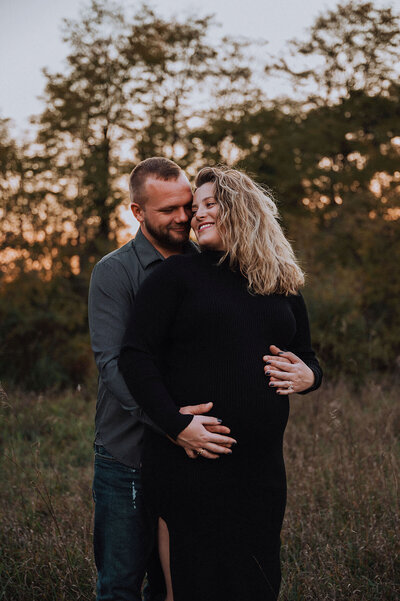 Husband and pregnant woman embracing one another in  a field at Kensington Metropark