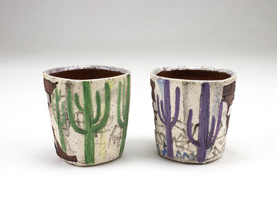 A ceramic cup that resembles plaster falling apart from red bricks with painted cacti and graffiti