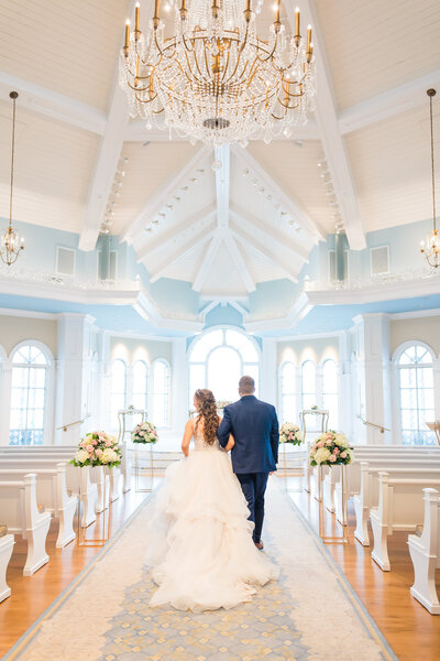 Bride and groom walking down the aisle in Disney's Wedding Pavilion. Wedding florals line the aisle of this beautiful wedding venue.