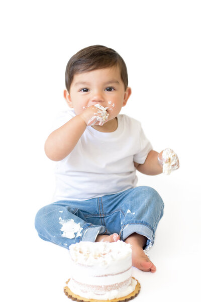 Little Boy in white shirt and jeans eating cake