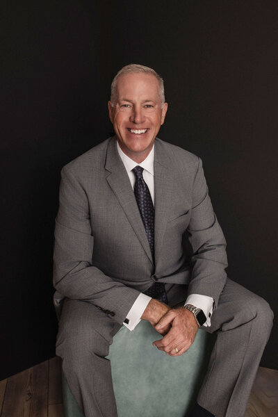 Mark Sullivan wearing a grey suite sitting on a green ottoman smiling – Life and Health Coach at LifeNBalance Coaching21