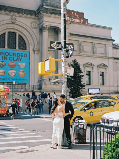 Engaged couple sharing an intimate moment in front of The Met Museum on 5th Avenue in New York City, surrounded by iconic yellow taxis and historic architecture, captured by Stephanie Michelle Photography, specializing in luxury wedding and engagement photography