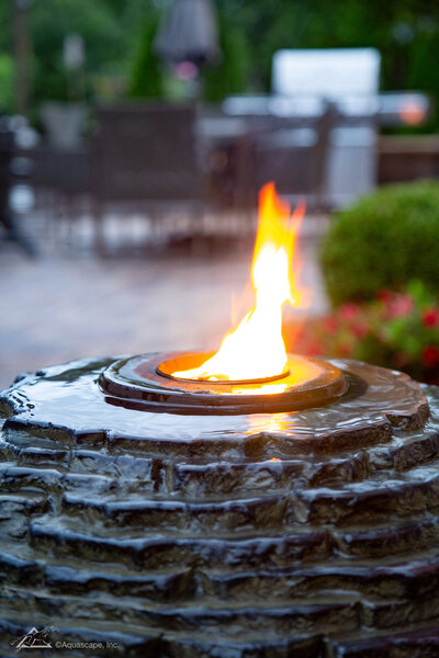 Stacked Slate Sphere fountain with running water and a fire flame glowing on top of the feature in the evening