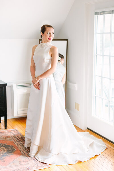 A brunette bride gazes out the window over her shoulder dressed in a high neck white wedding gown with a train