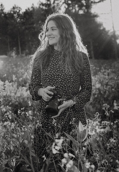 Johanna Schrag steht in einem Blumenfeld und hält eine Kamera.
