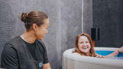 A breathwork instructor smiling as she guides a participant through an ice bath session, fostering resilience and calm under stress.