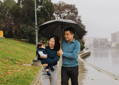 Mother and father standing with an umbrella and smiling down at their baby daughter