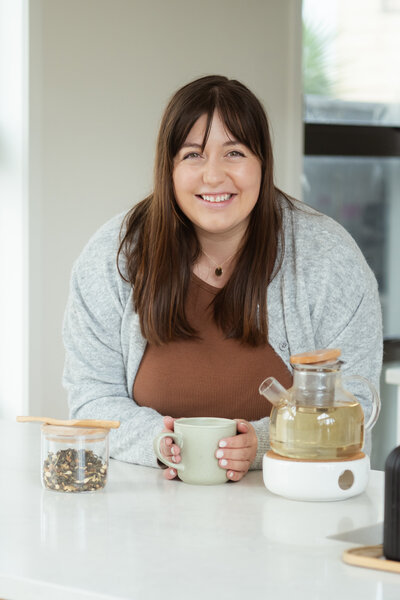 Chantal Hewitt smiling in brown shirt and grey sweater at kitchen island with a green mug - Family Autism Support Coach at Chantal Hewitt Coaching1