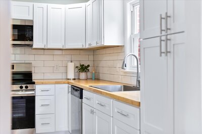 White kitchen with butcher block countertops, stainless steel appliances, and white tile backsplash.