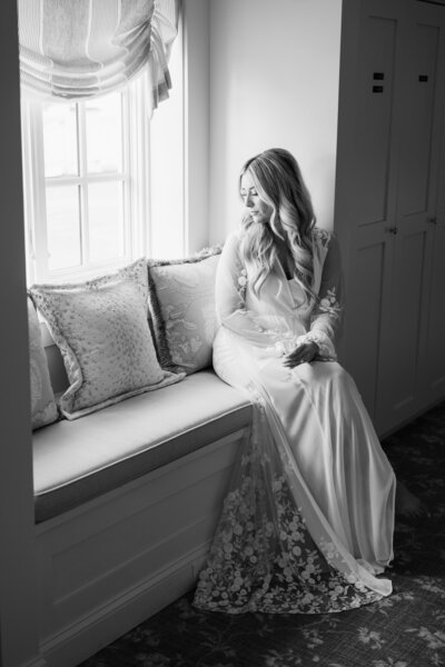 A bride sits near a window holding a glass of champagne in her bridal robe