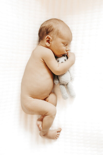 Sleeping infant lying on his side holding a grey teddy bear, taken from above, by lifestyle newborn photographer in Tifton, Georgia