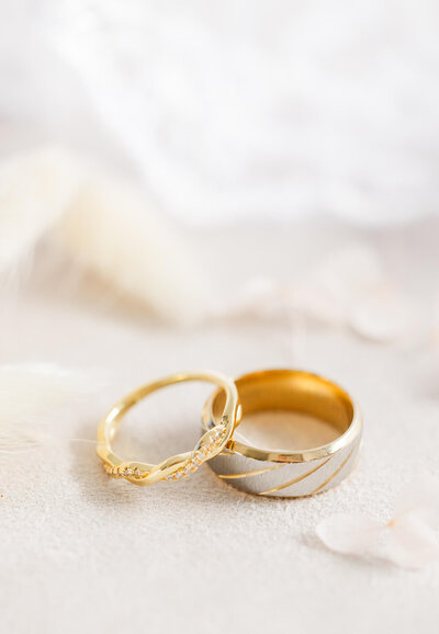 Bride and groom gold and diamond rings on a soft cream background.