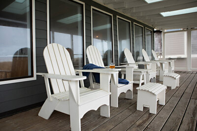 A Coastal home outdoor seating featuring white adirondack chairs, representing interior design and remodel by Winsome Home Interiors.