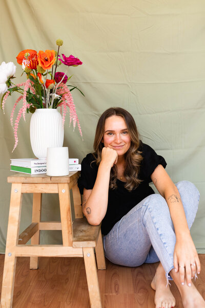 A woman smiling with a stack of graphic design books, a coffee, and a colorful bouquet of flowers.