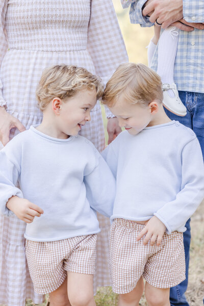 Twin boys in blue sweaters looking at one another.