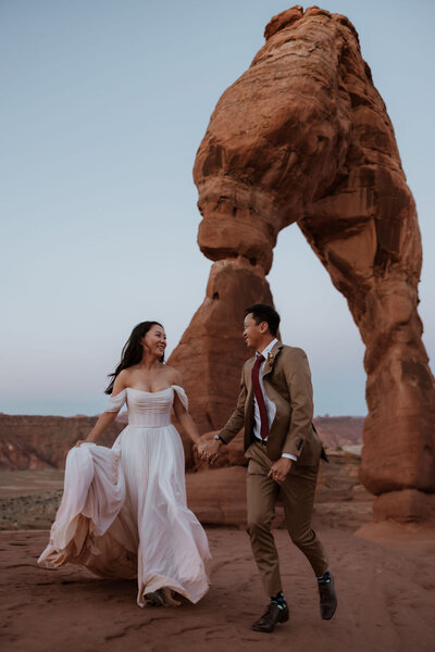 bride and groom walking towards arch in the desert