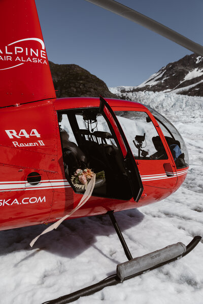 groom helping bride get out of a red helicopter on a glacier