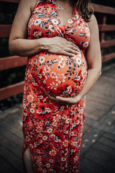 An Edmonton woman in an orange floral dress holding her pregnant belly.