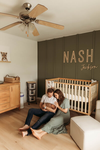 parents holding newborn baby while sitting on the floor of the nursery