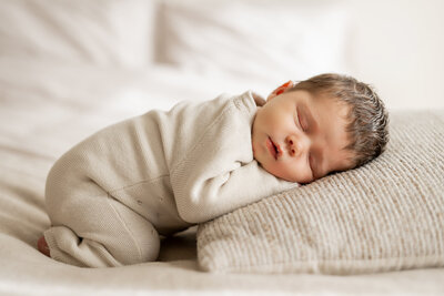 Slapende baby tijdens een newborn fotoshoot, liggend vredig op een zacht kussen – teder en puur vastgelegd door Juliette Fotografie.