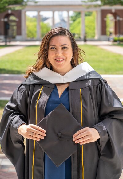 Woman dressed in her master's program cap and gown poses with one of the Johns Hopkins University's buildings behind her. Baltimore, Maryland