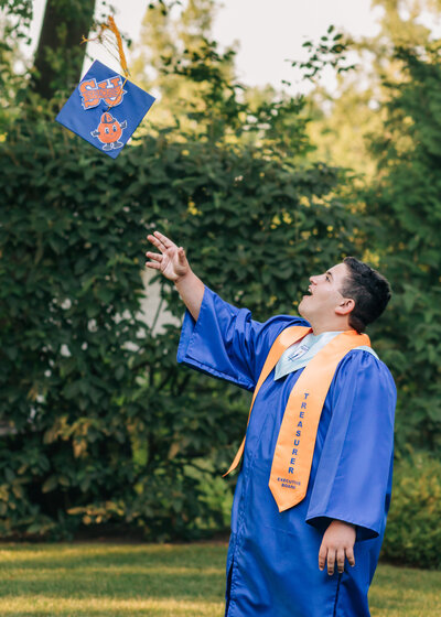 Man wearing graduation gown, throwing graduation cap in the air in NJ