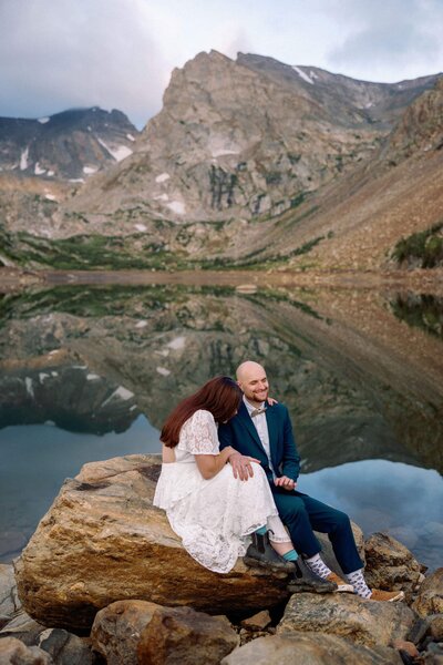 Bride and groom laugh while sitting lakeside during Colorado alpine lake mountain elopement.