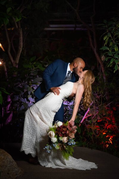 a groom dipping his bride in a butterfly pavilion 