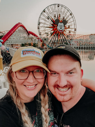 suzy goodrick and her husband pose in front the micket ferris wheel at disneyland