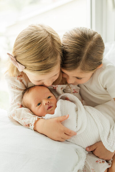 two sweet older siblings hold their newborn baby