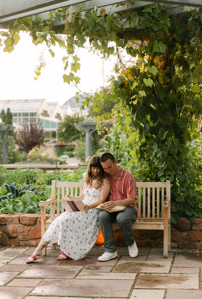 Couple reading a book on a bench under greenery at the Denver Botanic Gardens during their engagement session. 