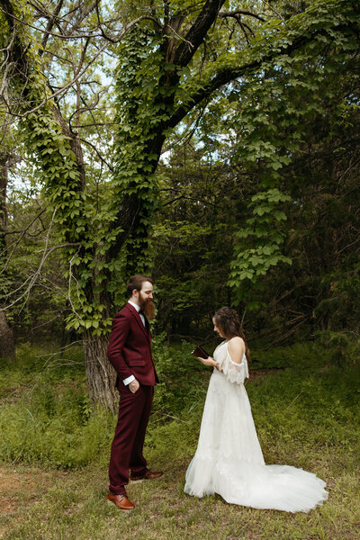 A couple standing in a wooded area reading notes to each other.