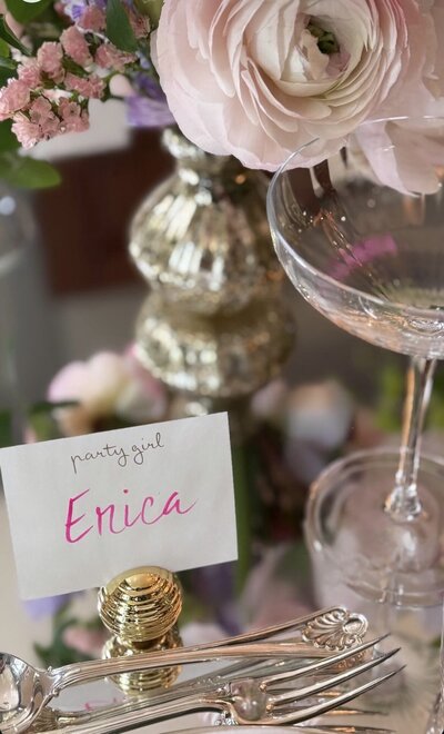 White place card with bright pink watercolor calligraphy in round gold stand. 