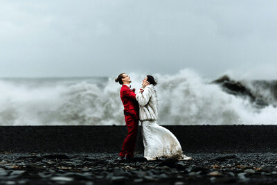 Married couple is celebrating their marriage in a storm with dramatic ocean waves in the background in Iceland