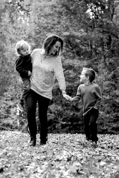 Mom holding hands with one kid while holding other child | Family Photography