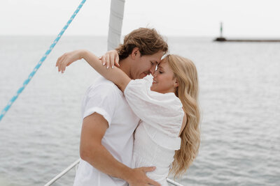 A couple with their arms around each other as they stand close on a sailboat 