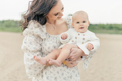 Photo of a smiling baby being held by mother in a light floral dress during an outdoor session in Kansas City