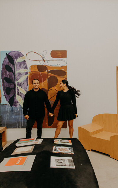 Real estate brokerage husband and wife Moises and Maria pose in front of art piece