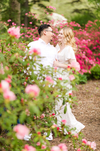 Young couple posing for engagement photo in pink bushes