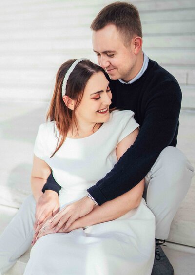 woman sits in between man's legs on the stair during their engagement session at supreme court in Washington D.C.