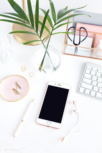 Photo of rose gold and white iphone with earbuds sitting on a desk