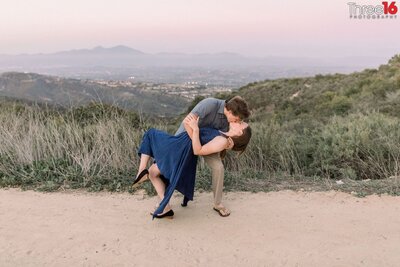 Groom to be dips his future Bride and kisses her while on a dirt trail at Top of the World in Laguna Niguel