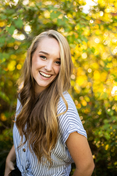 Teen girl poses for senior photos outside in blue and white striped blouse