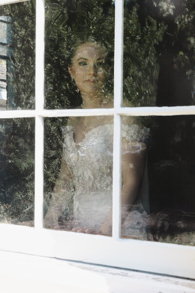 A person in a wedding dress looking out of a window taken from outside 
